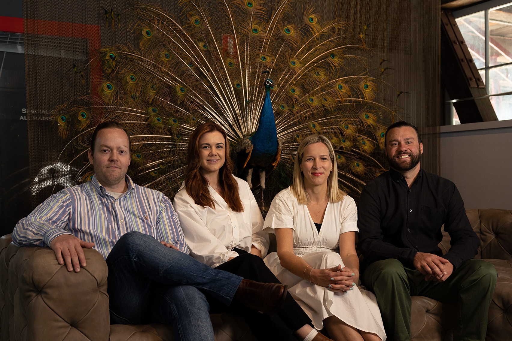 Marcus Layman, Kate LeMoine, Jessica Torstensson and Rick Sillan sitting on couch on the Sydney office with a peacock behind them