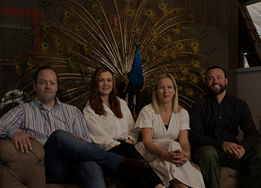 Marcus Layman, Kate LeMoine, Jessica Torstensson and Rick Sillan sitting on couch on the Sydney office with a peacock behind them